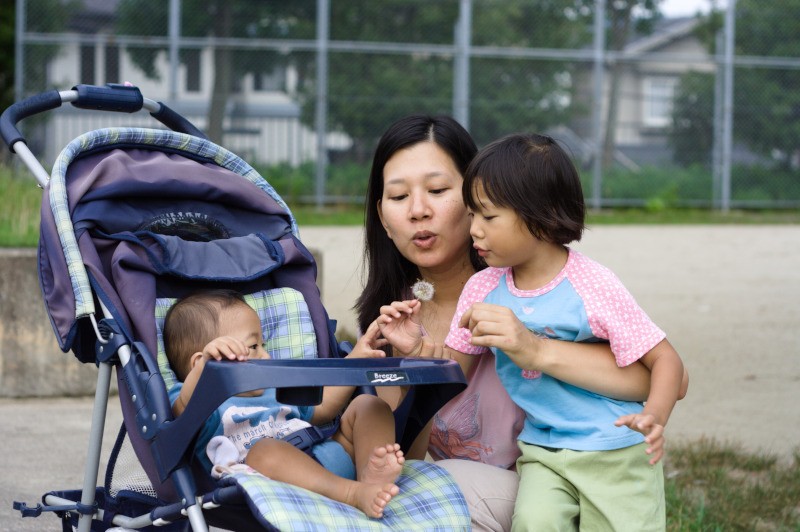 mother and daughter showing baby how to blow on a dandelion