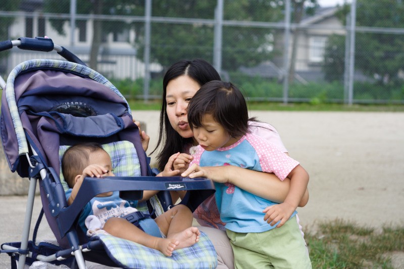 mother and toddler daughter showing baby how to blow on a dandelion
